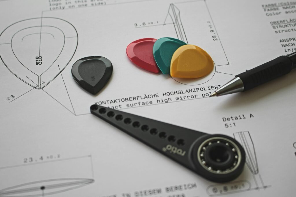 pexels-photo-6444715-6444715 Colorful guitar picks on a technical design blueprint with pen and tool.